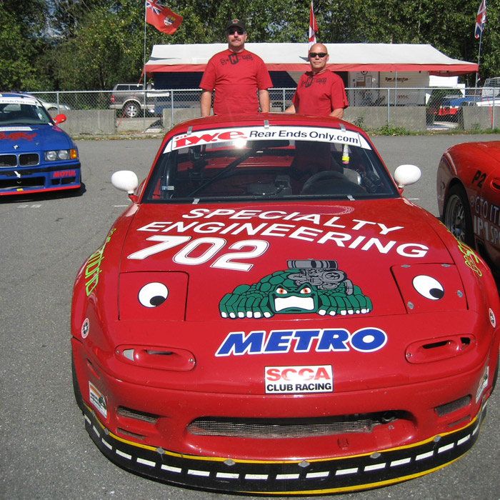 Harry Watson and his crew chief pose behind his red Mazda Miata race car